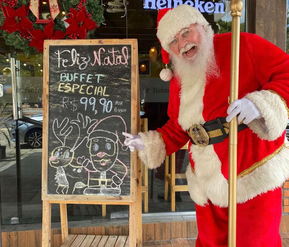 Papai Noel ao lado de um quadro de Feliz Natal na entrada do restaurante