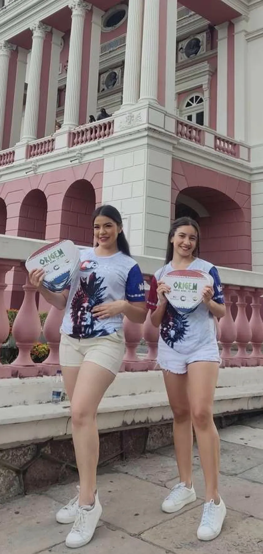 Duas promotoras com leques da marca em frente a um prédio histórico de Manaus